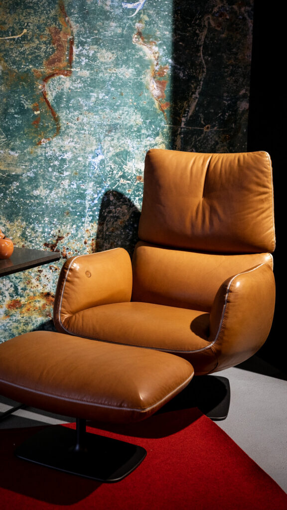 Cognacfarbener Leder-Loungesessel mit Hocker vor einer Steinwand