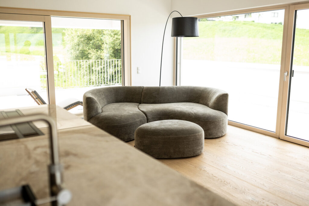 Grün-graues Rundsofa mit Hocker in einem hellen Wohnraum mit Eichenboden